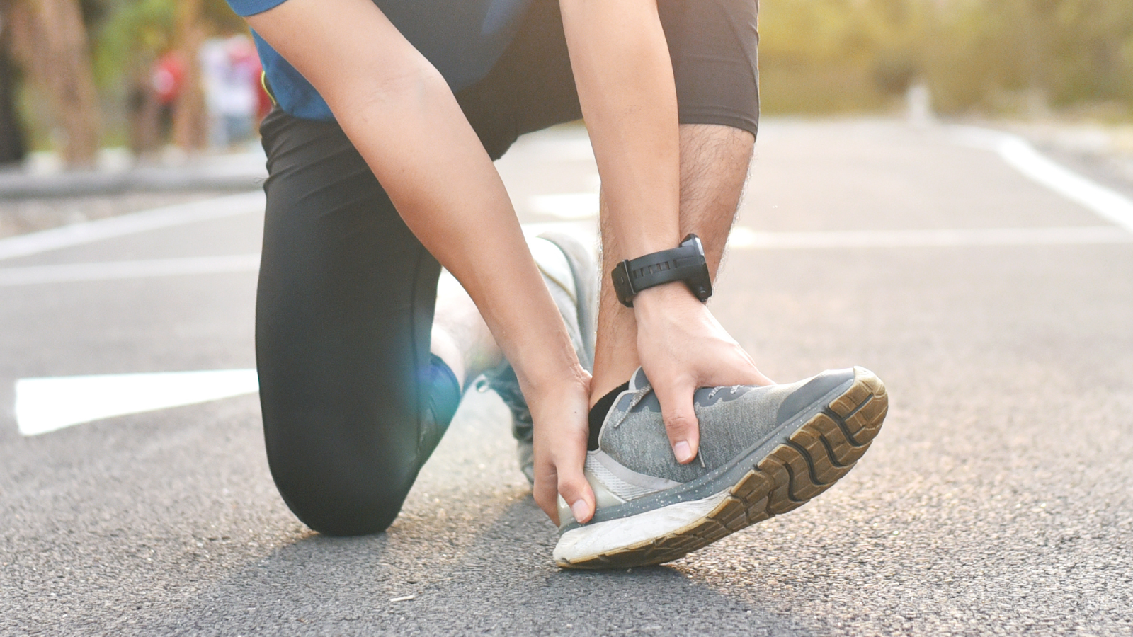 Runner holding his ankle after an injury on the road, indicating a possible ankle sprain.