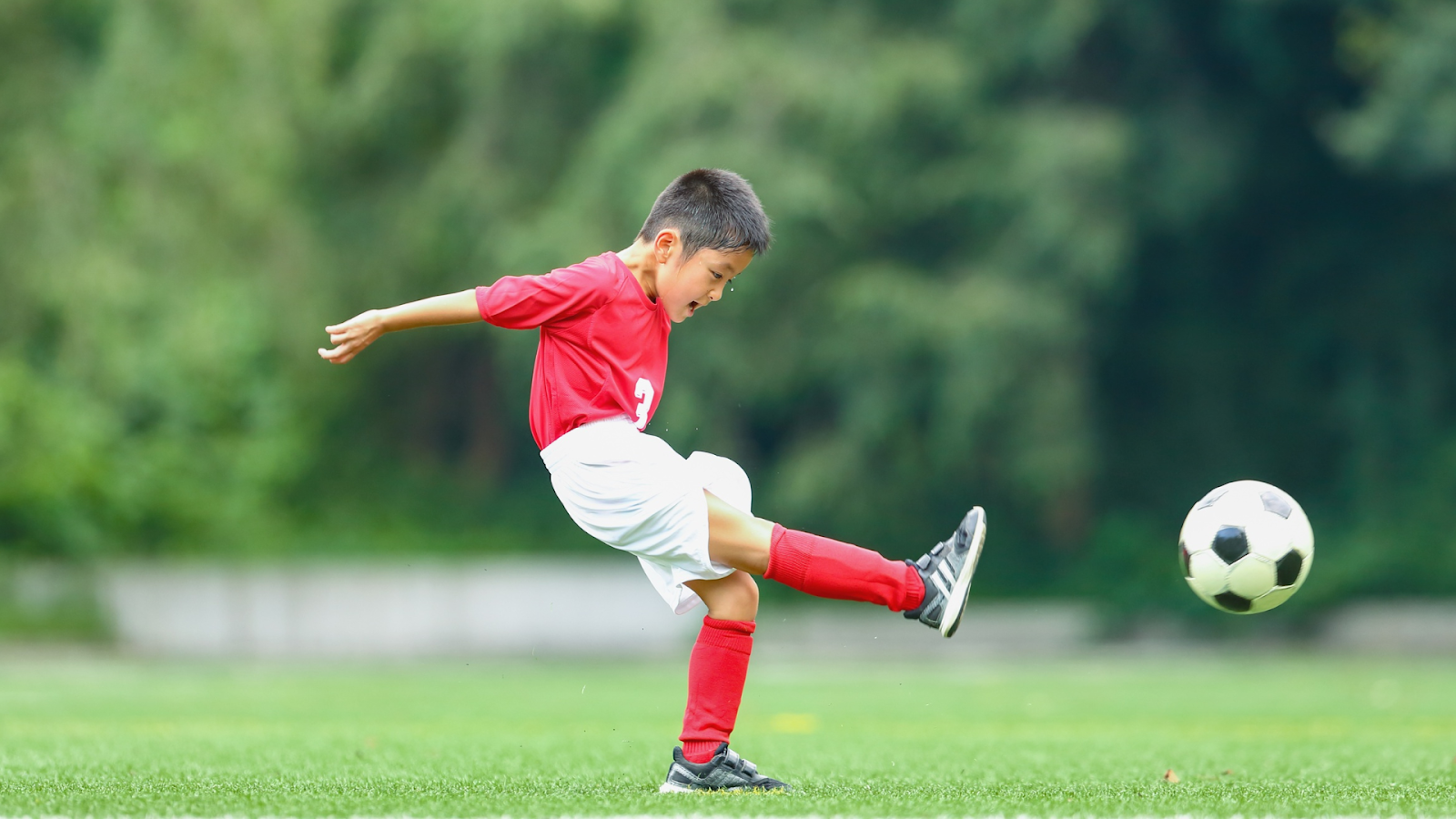Child playing soccer and kicking a ball – sports can trigger Osgood-Schlatter’s Disease symptoms.
