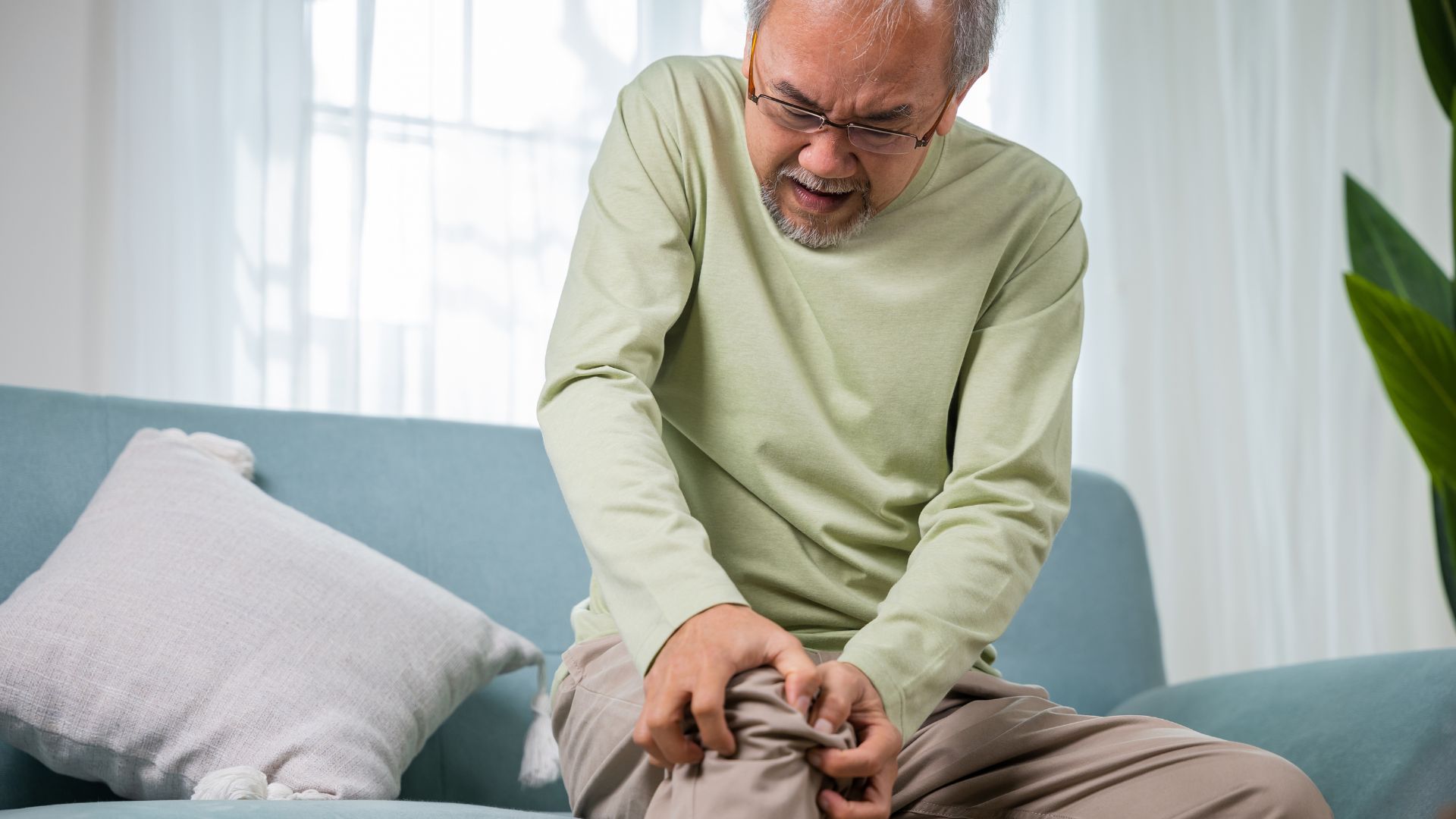 Elderly man experiencing knee pain at home, showing signs of rheumatoid arthritis affecting his mobility