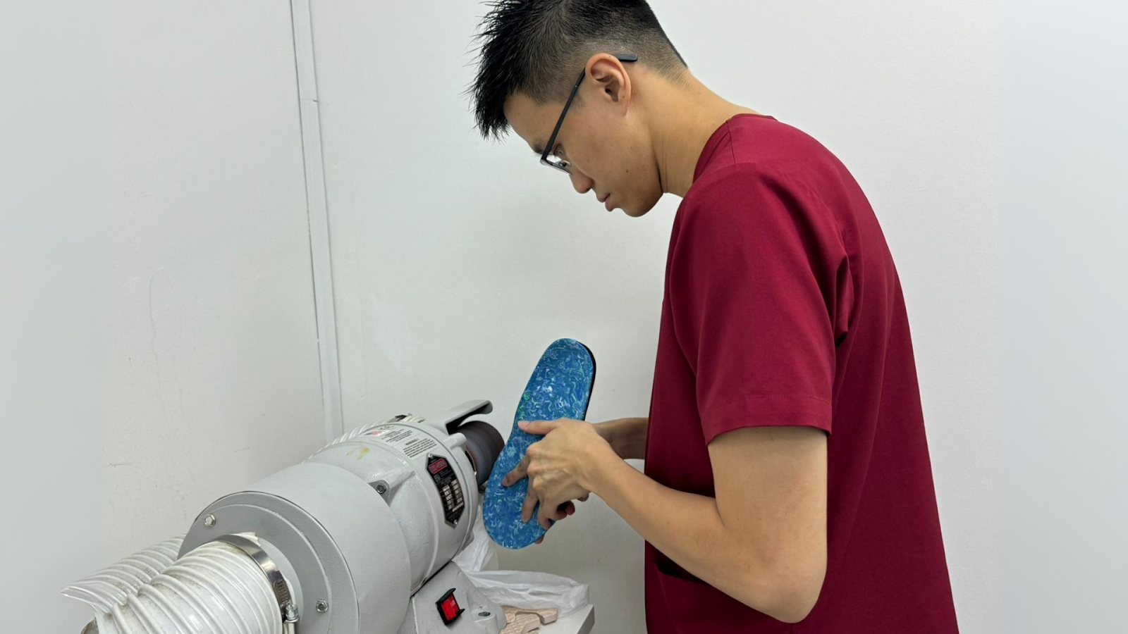 Specialist shaping a blue orthotic insole using a grinding machine.