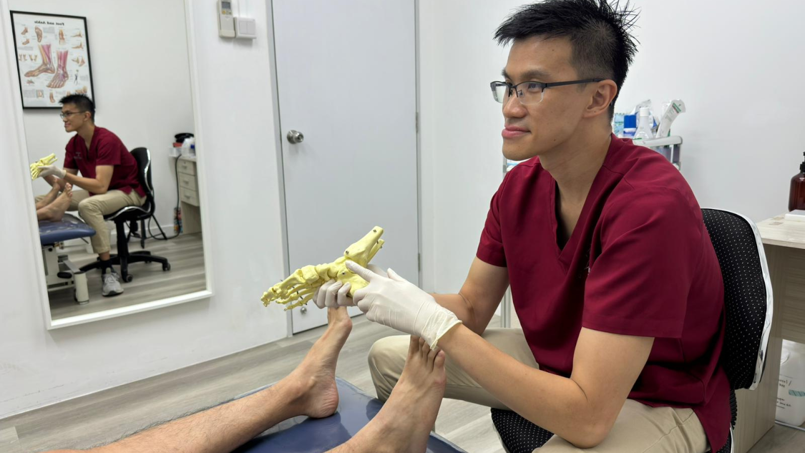 Alt text: Podiatrist showing a foot skeleton model during a custom orthotics consultation in Singapore