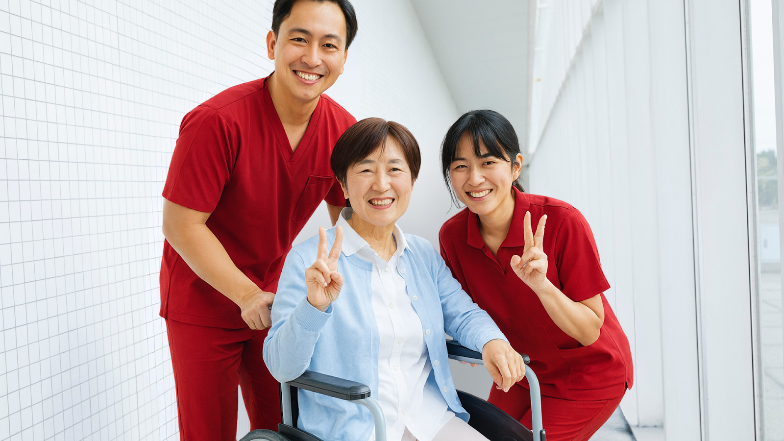Patient in wheelchair with two caregivers smiling, celebrating progress in rehab post-surgery.