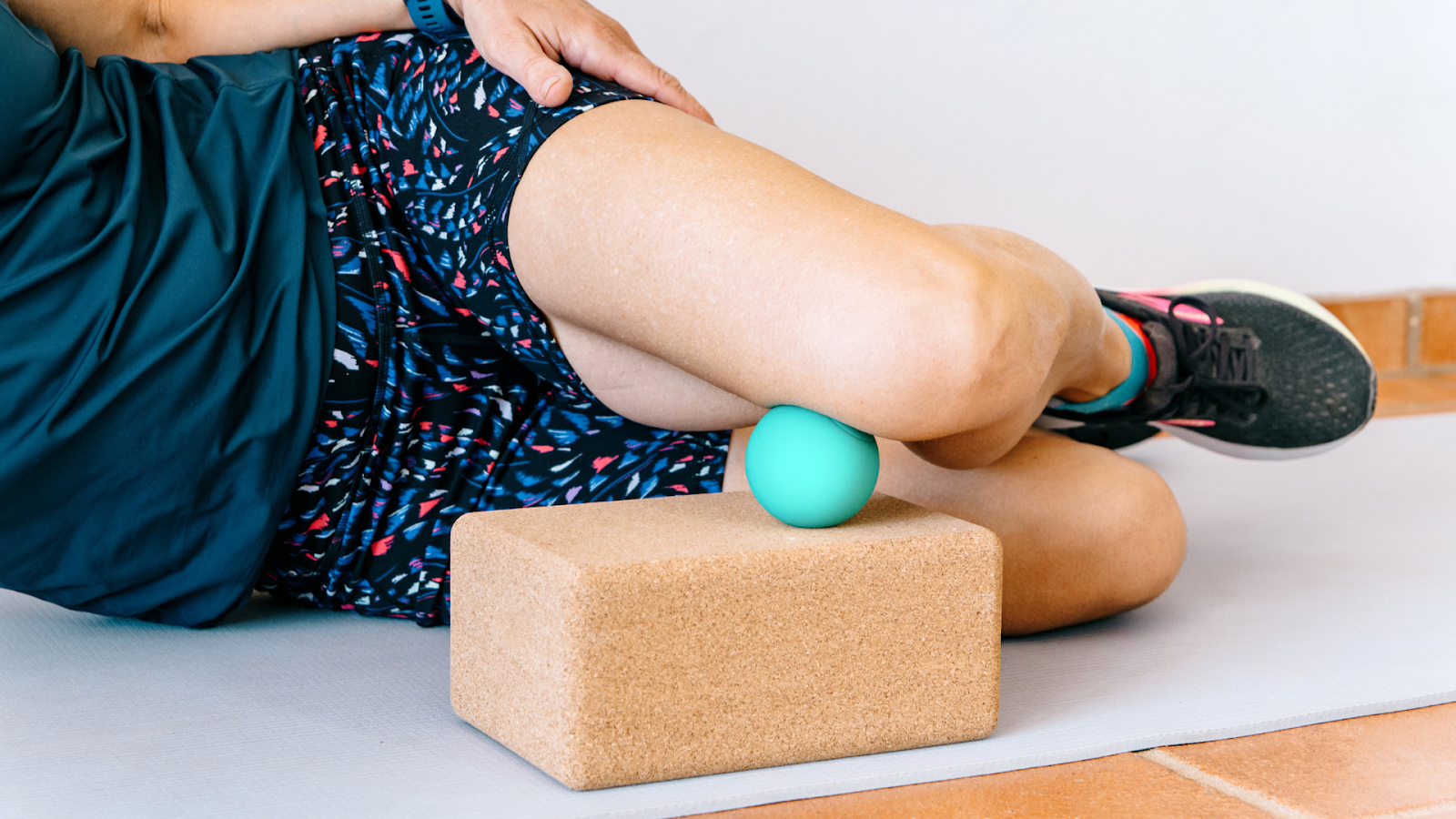 Runner performing self-myofascial release on the outer thigh using a massage ball and yoga block, part of a recovery routine to prevent foot and leg injuries in marathon training.