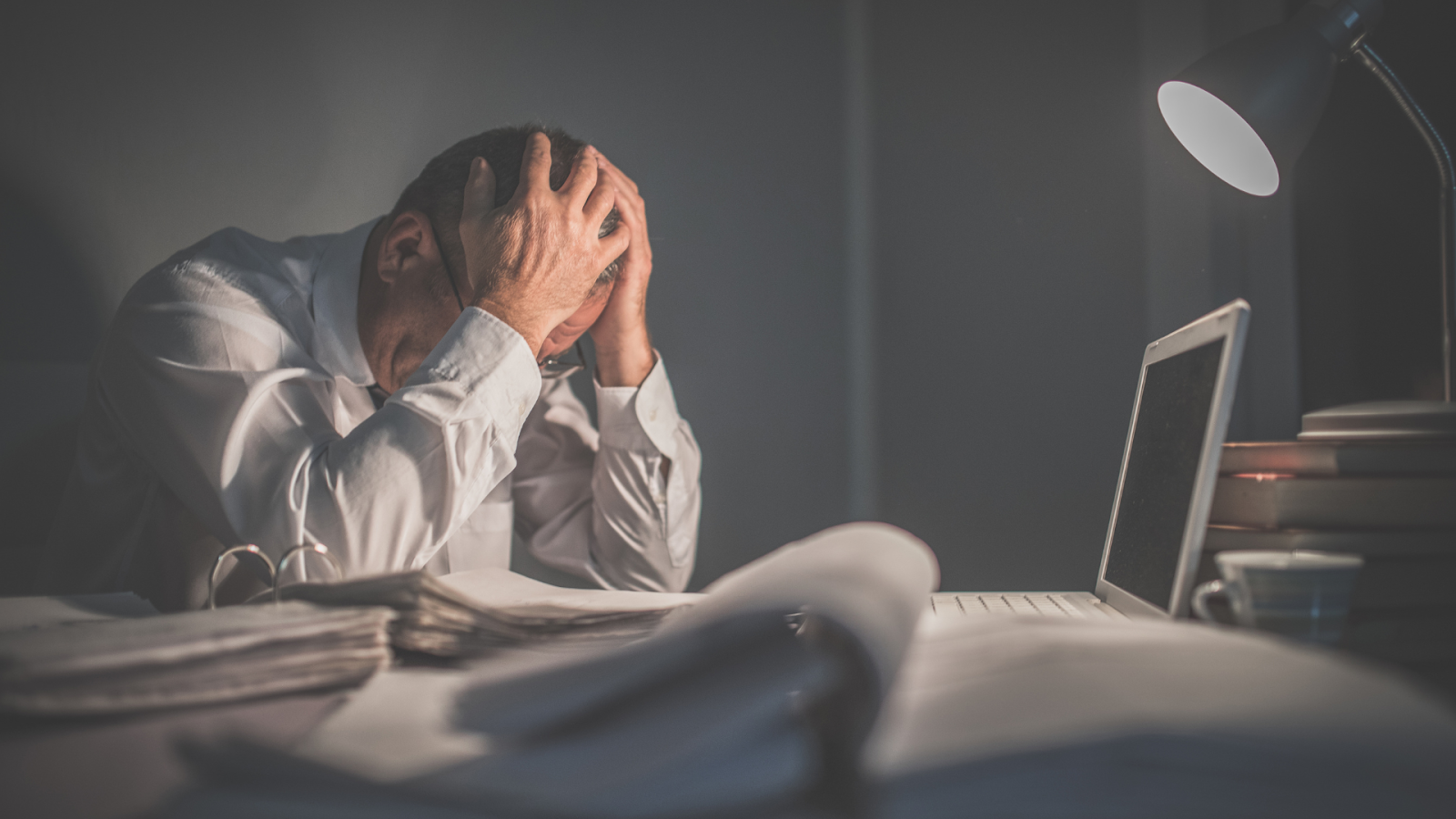 Older man feeling overwhelmed at his desk, possibly due to chronic pain or undiagnosed rheumatoid arthritis