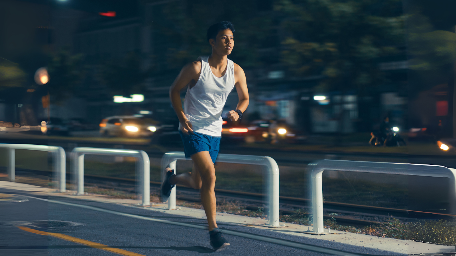Young man running at night on a Singapore street with blurred city lights in the background.