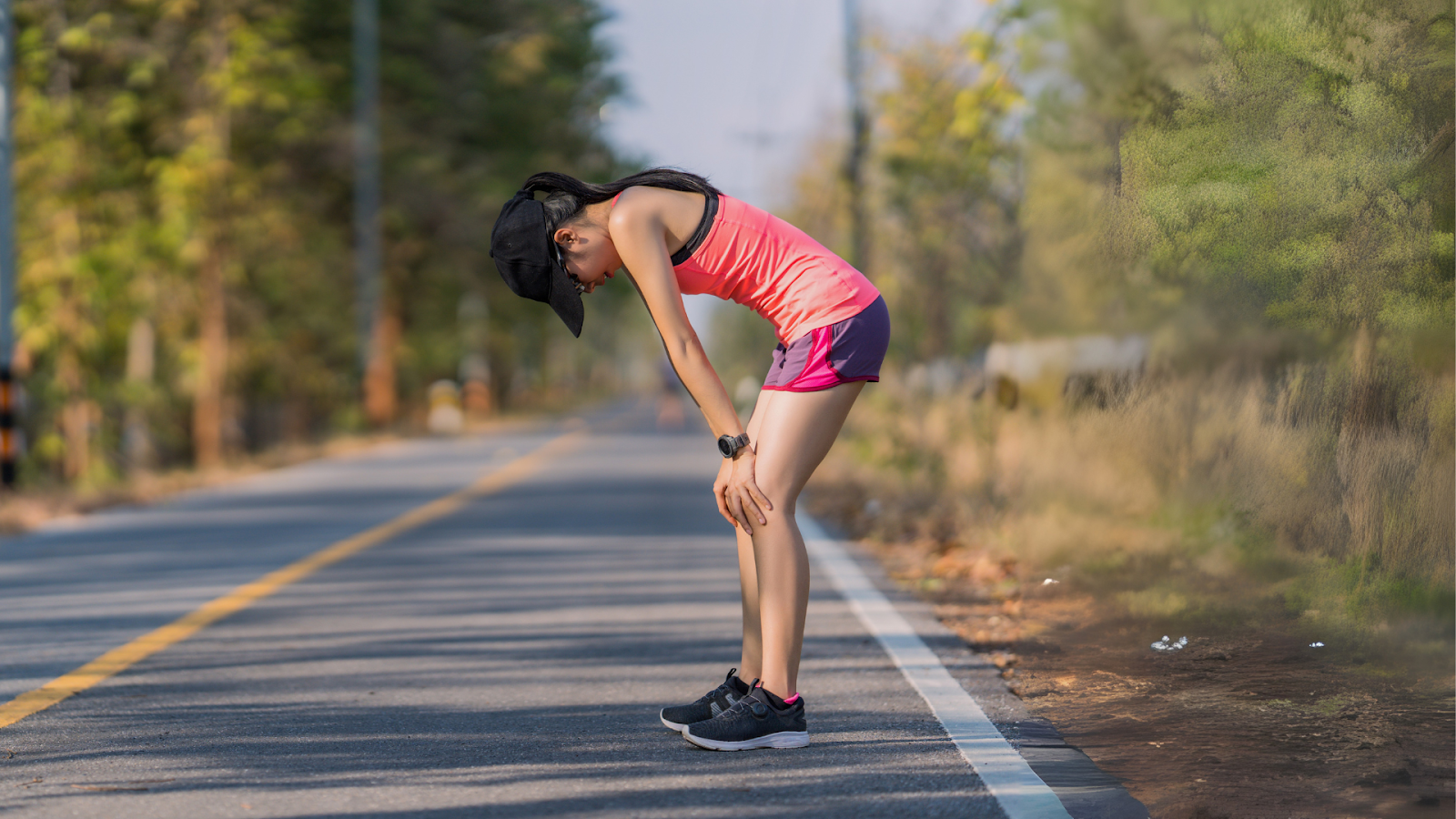 Female runner in athletic gear resting on the roadside, appearing fatigued during a long-distance run — illustrating the physical toll of marathon running and the need for proper training and foot care in Singapore.