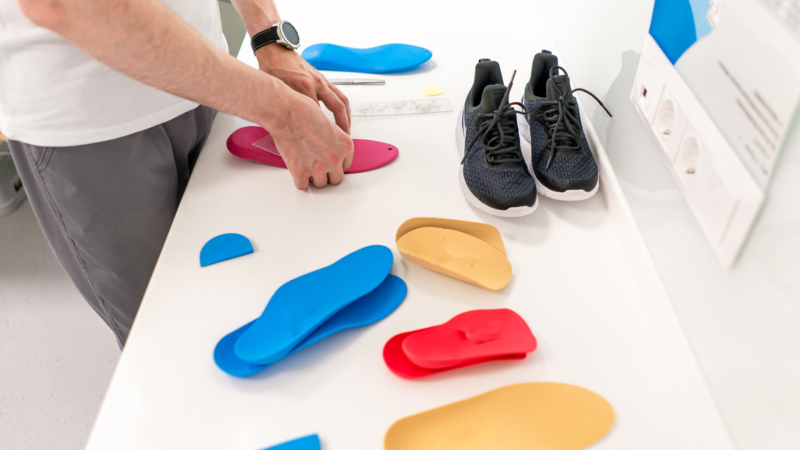 Professional working on custom orthotics in a clinic, with various insole shapes on the table.