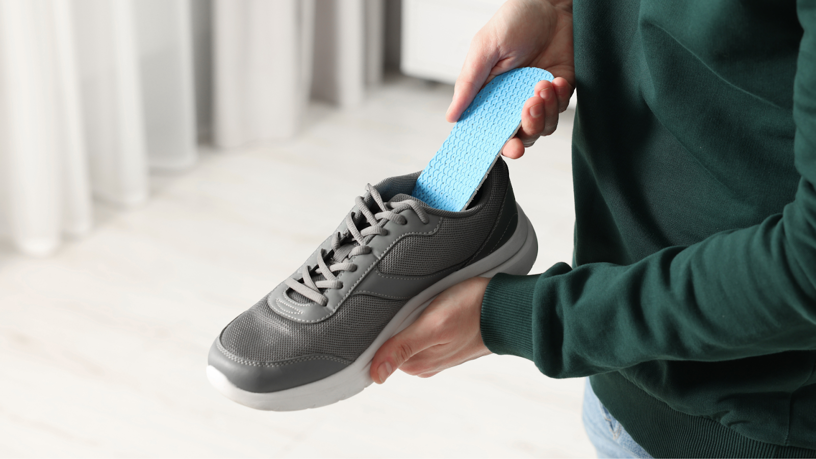 Person inserting a blue orthotic insole into a grey sports shoe.