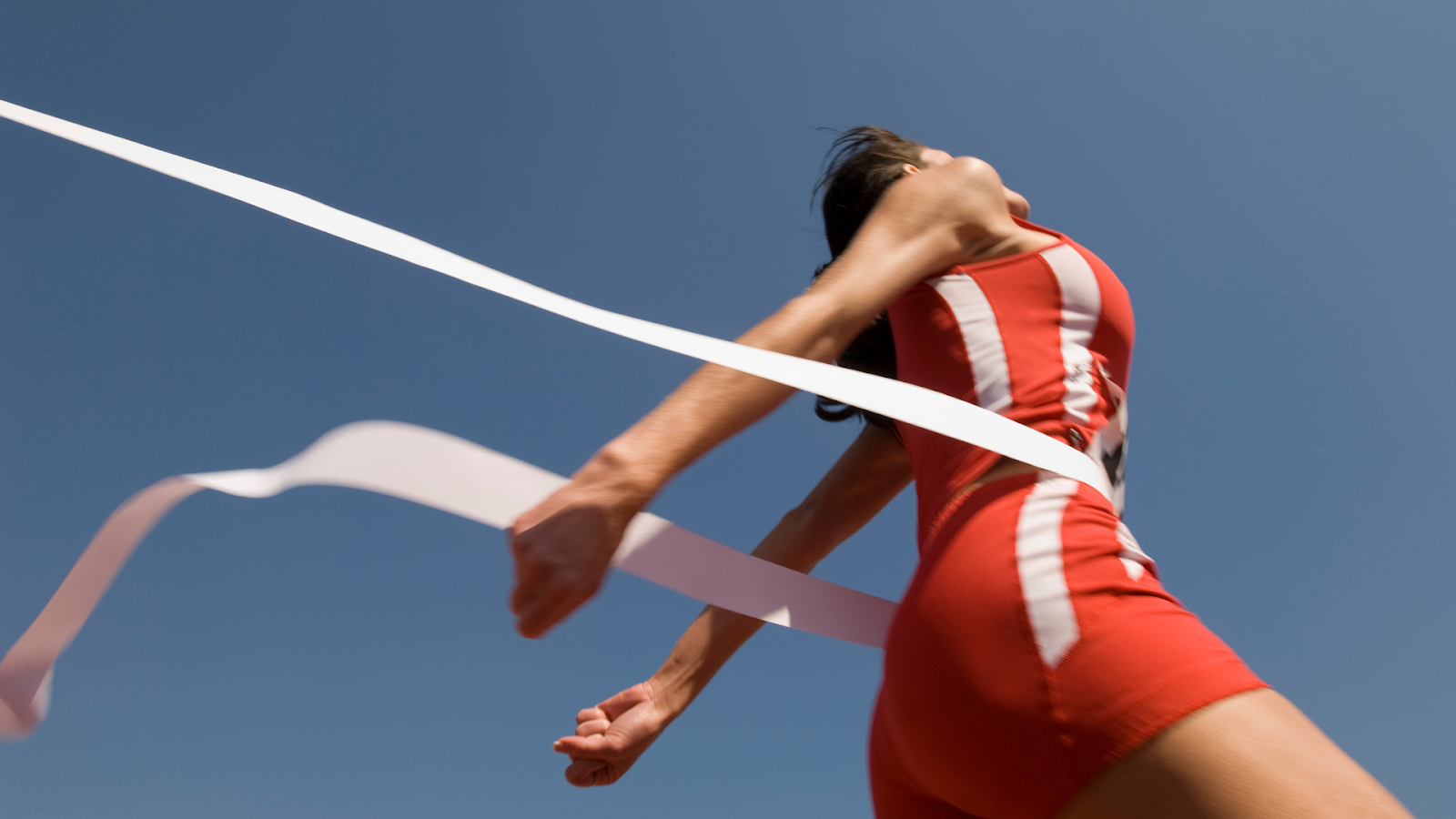 Female runner in red athletic gear crossing the finish line with arms extended, symbolising achievement and the culmination of training and foot care efforts in a marathon.