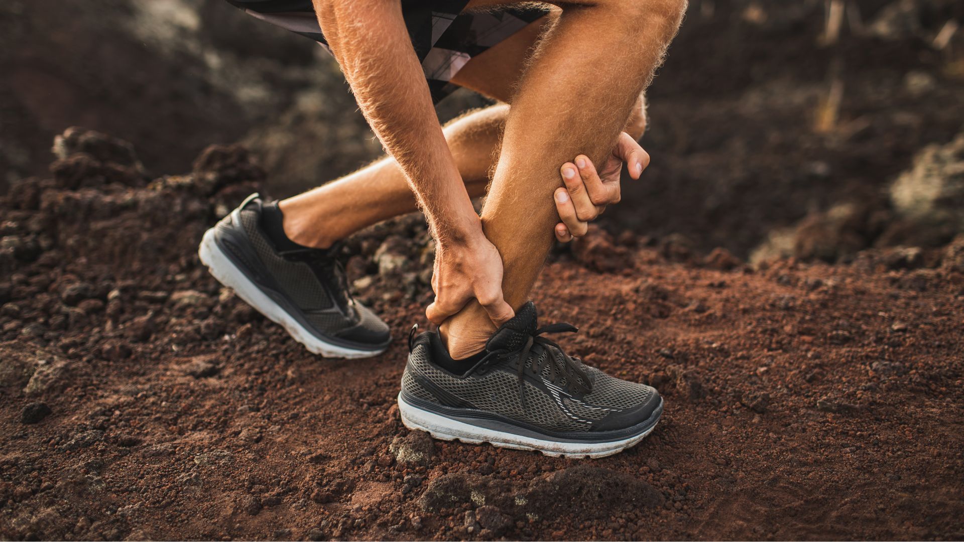 Male runner outdoors holding ankle in pain, representing sudden Achilles tendonitis flare-up.