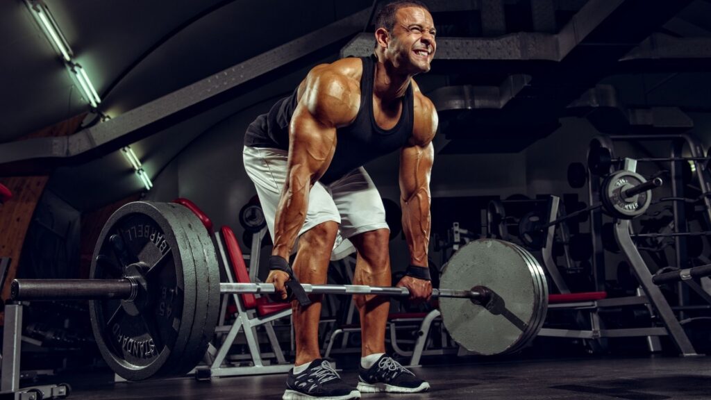 Muscular man performing an intense deadlift in a gym, highlighting strain on muscle groups and potential need for recovery interventions like dry needling.