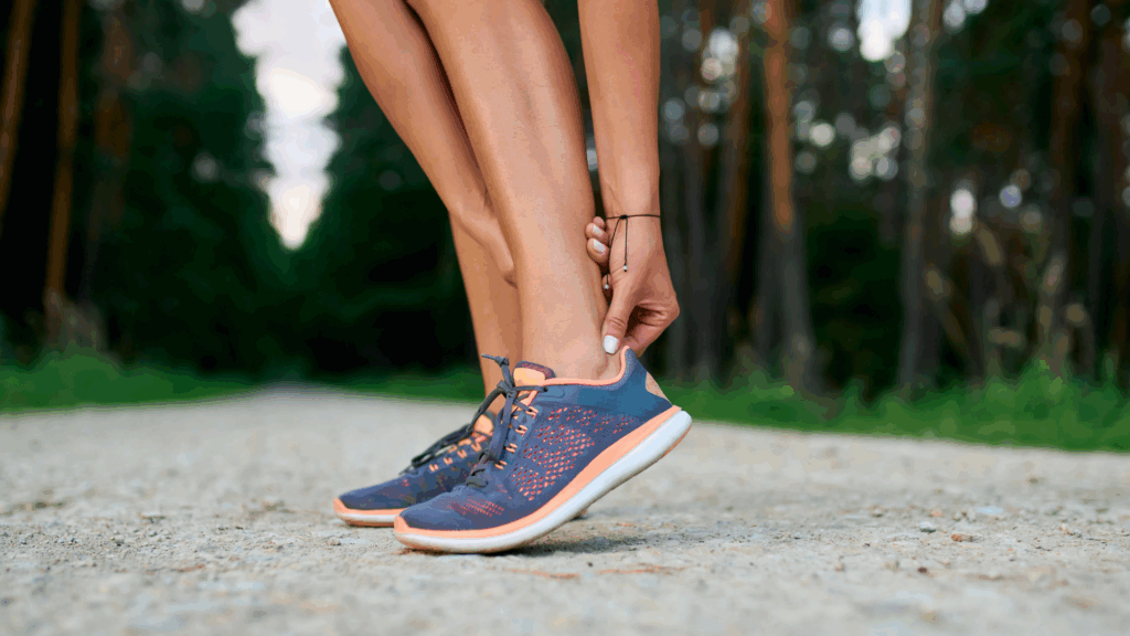Female runner stopping to hold her Achilles tendon due to heel pain, a common sign of Achilles tendonitis.