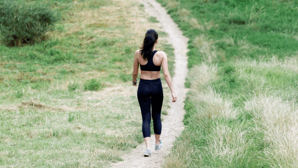 Woman walking on a grassy trail, demonstrating a safe, low-impact alternative for Achilles tendonitis recovery.