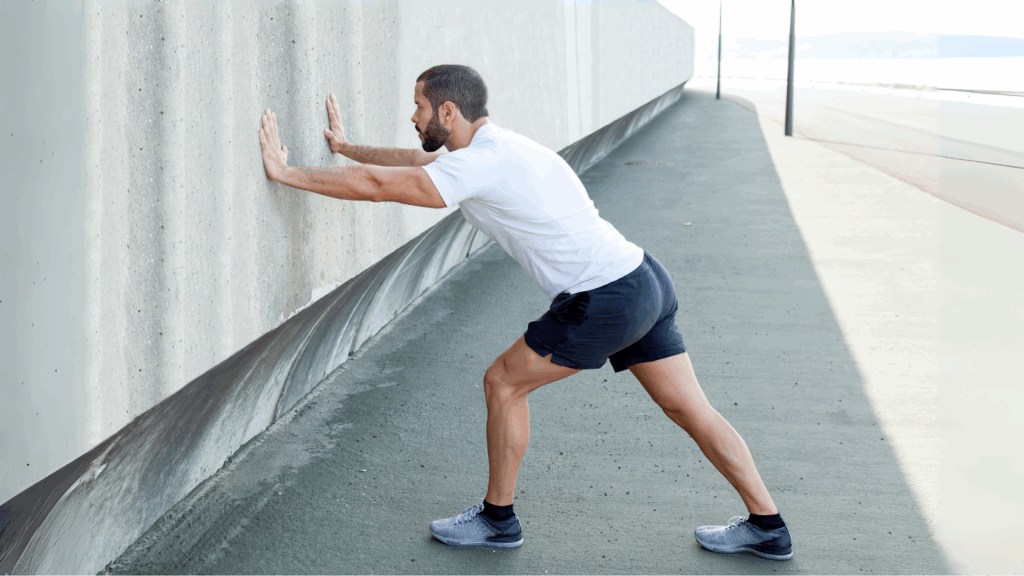 Male runner doing a wall calf stretch to relieve tightness and support Achilles tendon rehabilitation.