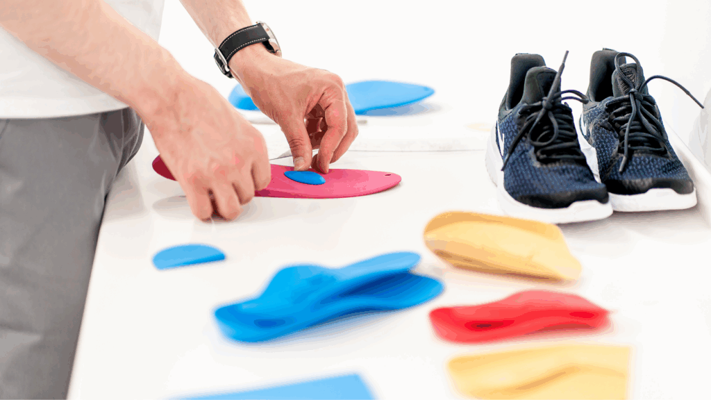 Person adjusting colourful orthotic insoles beside a pair of sports shoes on a white table.