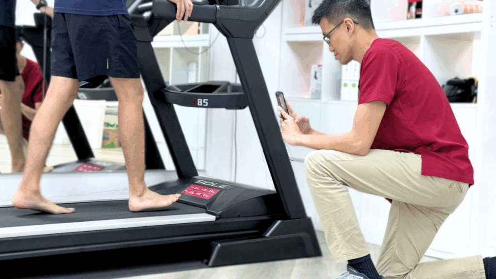 Physiotherapist performing gait analysis by filming a patient walking barefoot on a treadmill.