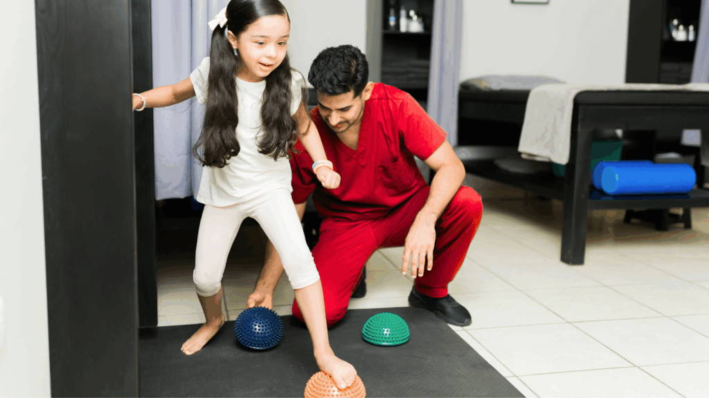 Young girl balancing barefoot on spiky therapy balls under supervision of a physiotherapist.