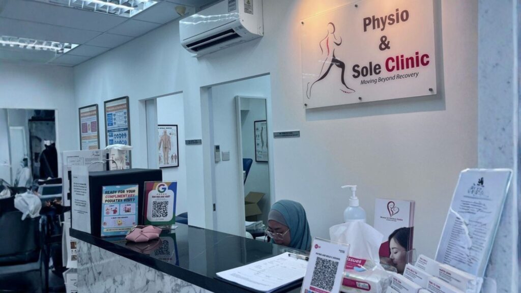 Reception area of Physio & Sole Clinic Kovan featuring the clinic’s logo on the wall, informational brochures, and a friendly staff member at the front desk in a clean, professional setting.