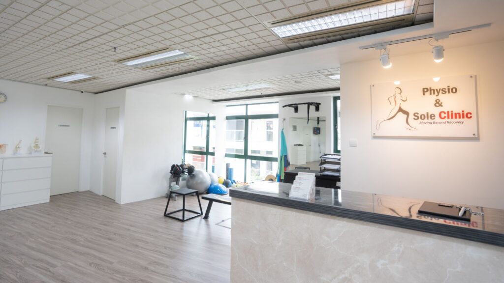 Bright and spacious interior of Physio & Sole Clinic Jurong featuring the reception counter, clinic logo, and physiotherapy equipment like exercise balls and weights in a clean, modern environment.
