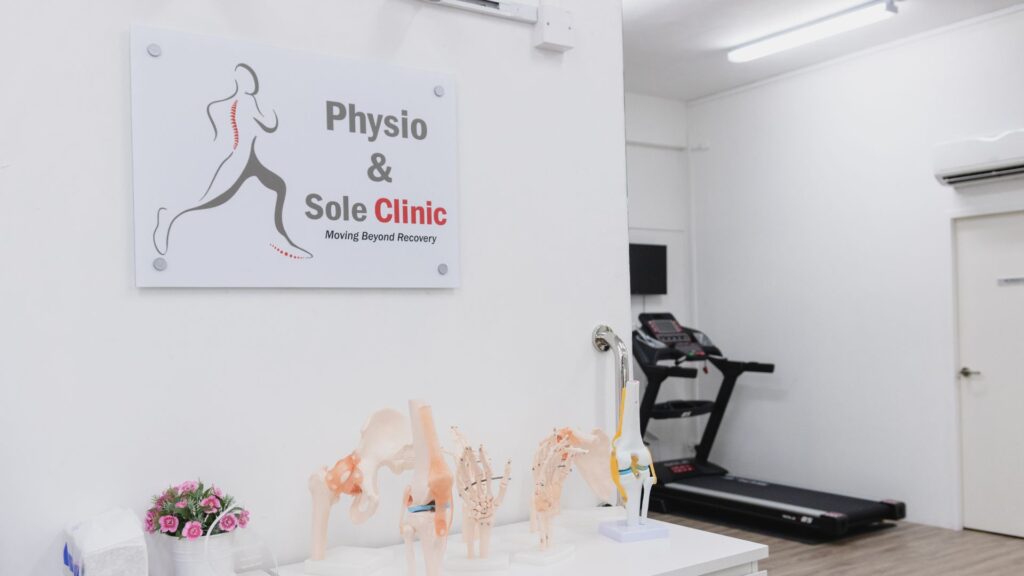 Interior of Physio & Sole Clinic Yishun featuring anatomical joint models, the clinic’s logo on the wall, and a treadmill in a bright, clean rehabilitation space.