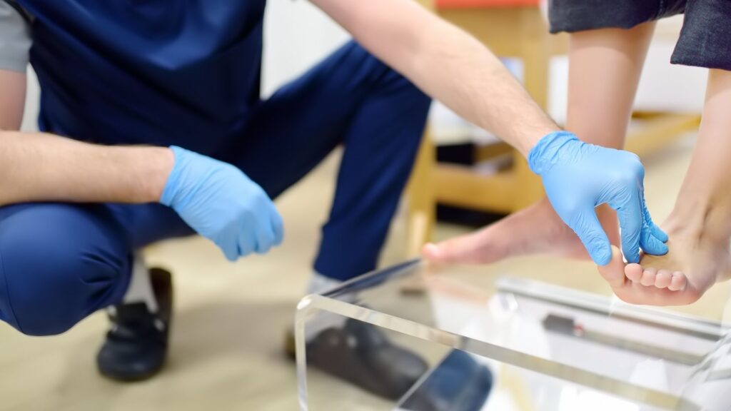 Podiatrist in clinic assessing patient’s foot alignment before prescribing custom orthotics