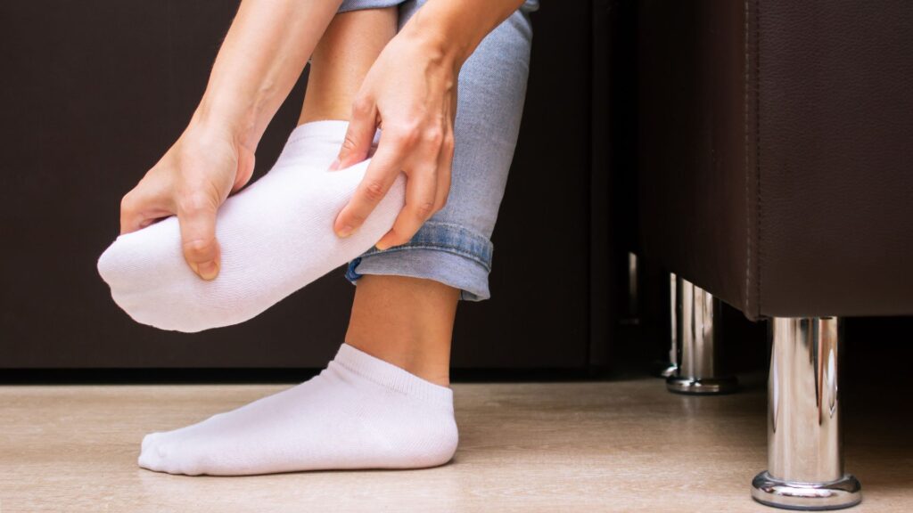 Person touching heel through sock showing common heel pain relieved by orthotics