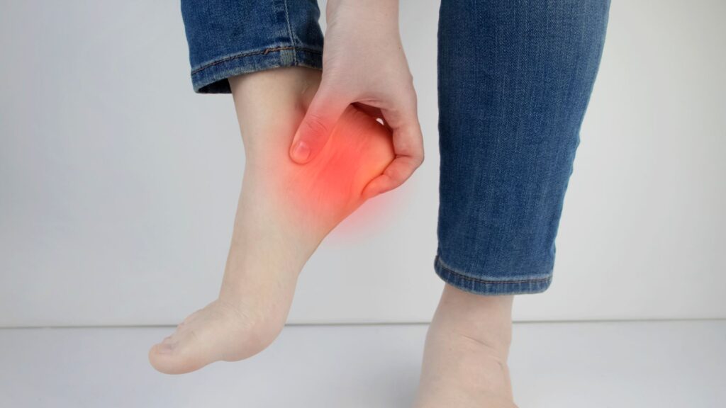 Person holding heel with red pain highlight, showing plantar fasciitis or heel pain before shockwave treatment.