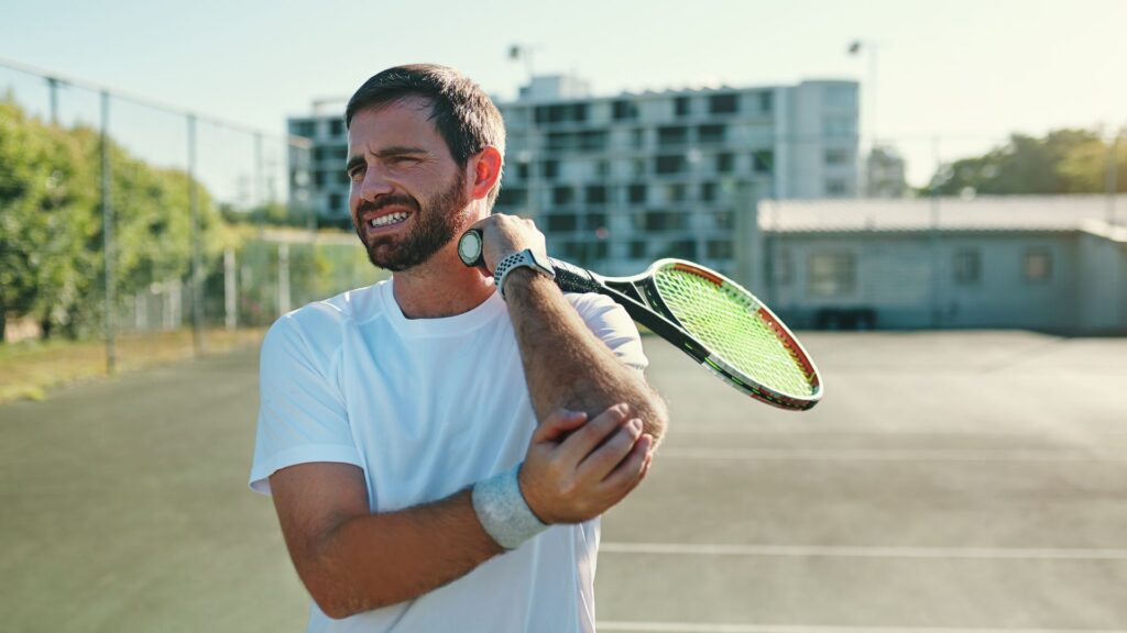 Male tennis player holding elbow in pain from tennis elbow, a condition often treated with shockwave therapy.