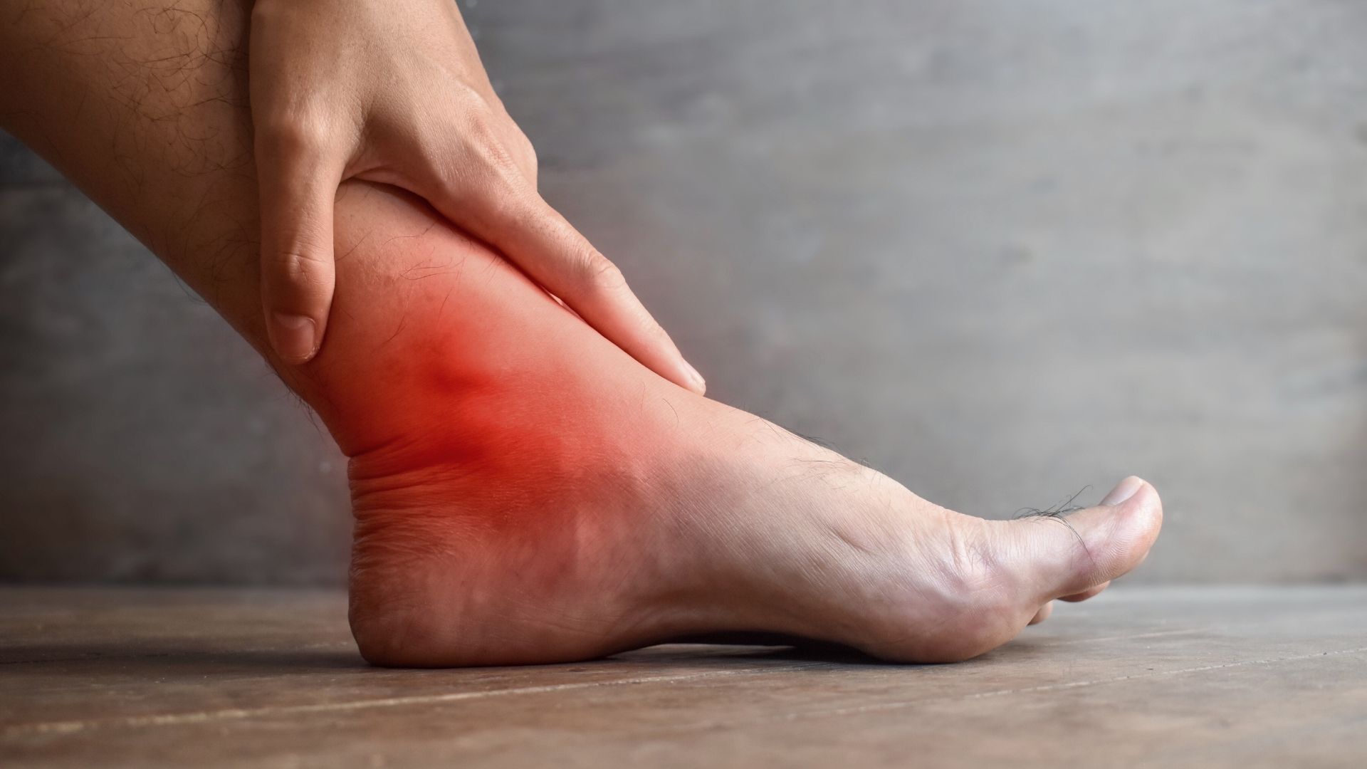 A person holding their heel with visible redness, showing common pain associated with high-arched feet such as plantar fasciitis or heel strain.