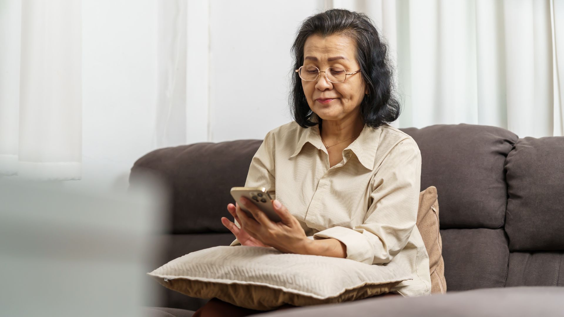 An older woman sitting on a sofa using her phone, representing individuals learning about chronic foot pain or high-arched feet symptoms.