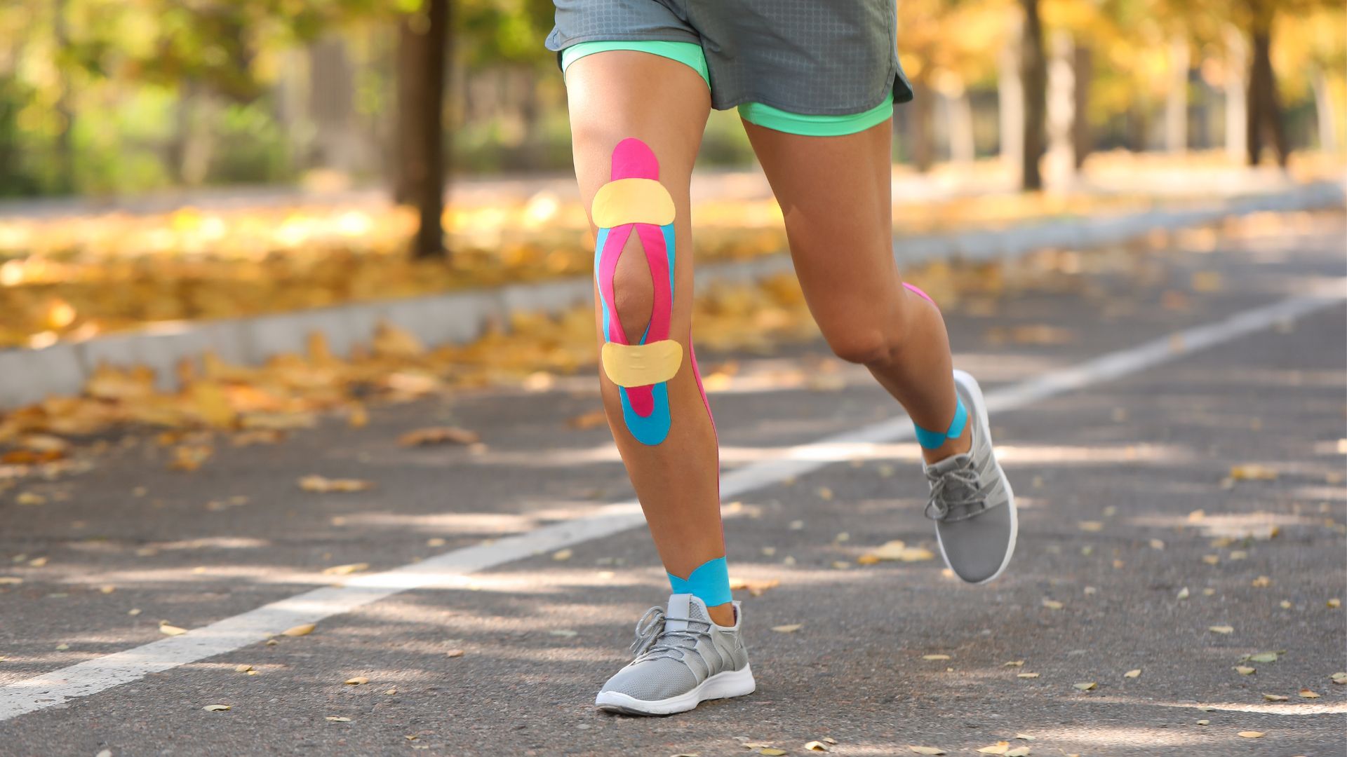 A runner with colourful kinesiology tape applied on the knee while running outdoors for injury support.