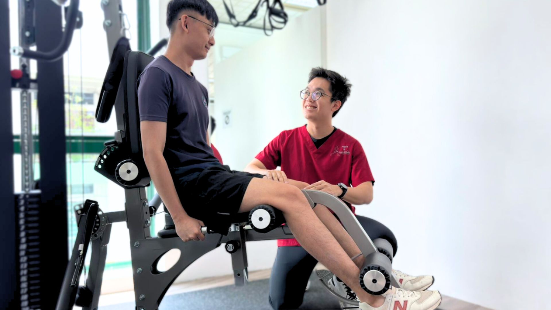 A physiotherapist supervising a patient using a leg strengthening machine during rehab training in a clinic.