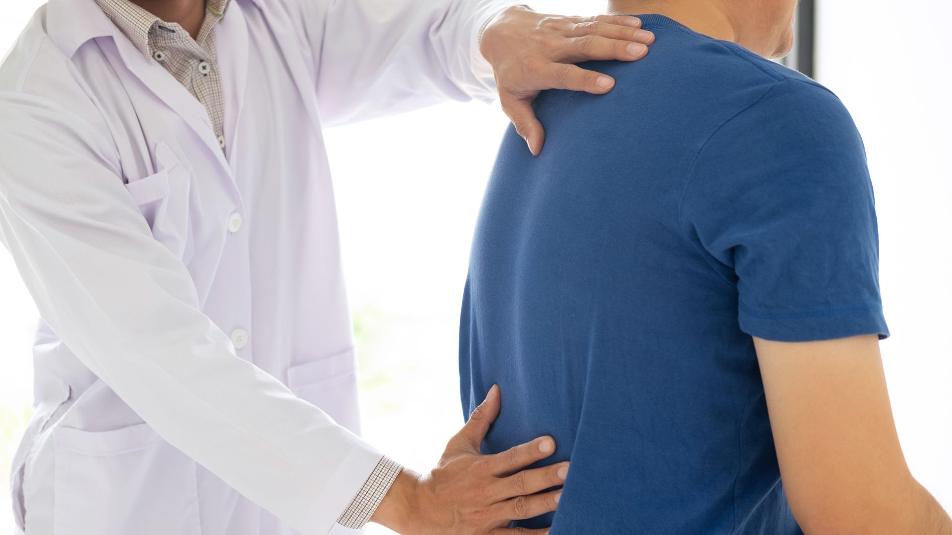 A physiotherapist performing a hands-on lower back assessment on a patient wearing a blue shirt during a clinical physiotherapy session.