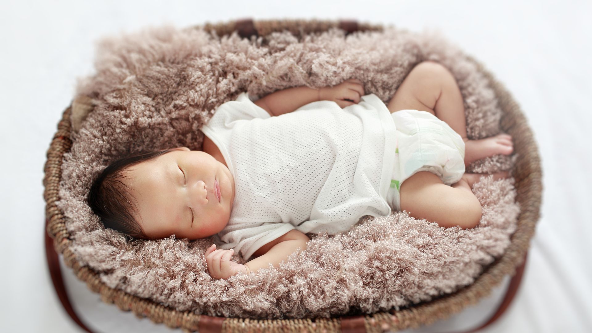 Newborn baby sleeping peacefully in a soft basket.