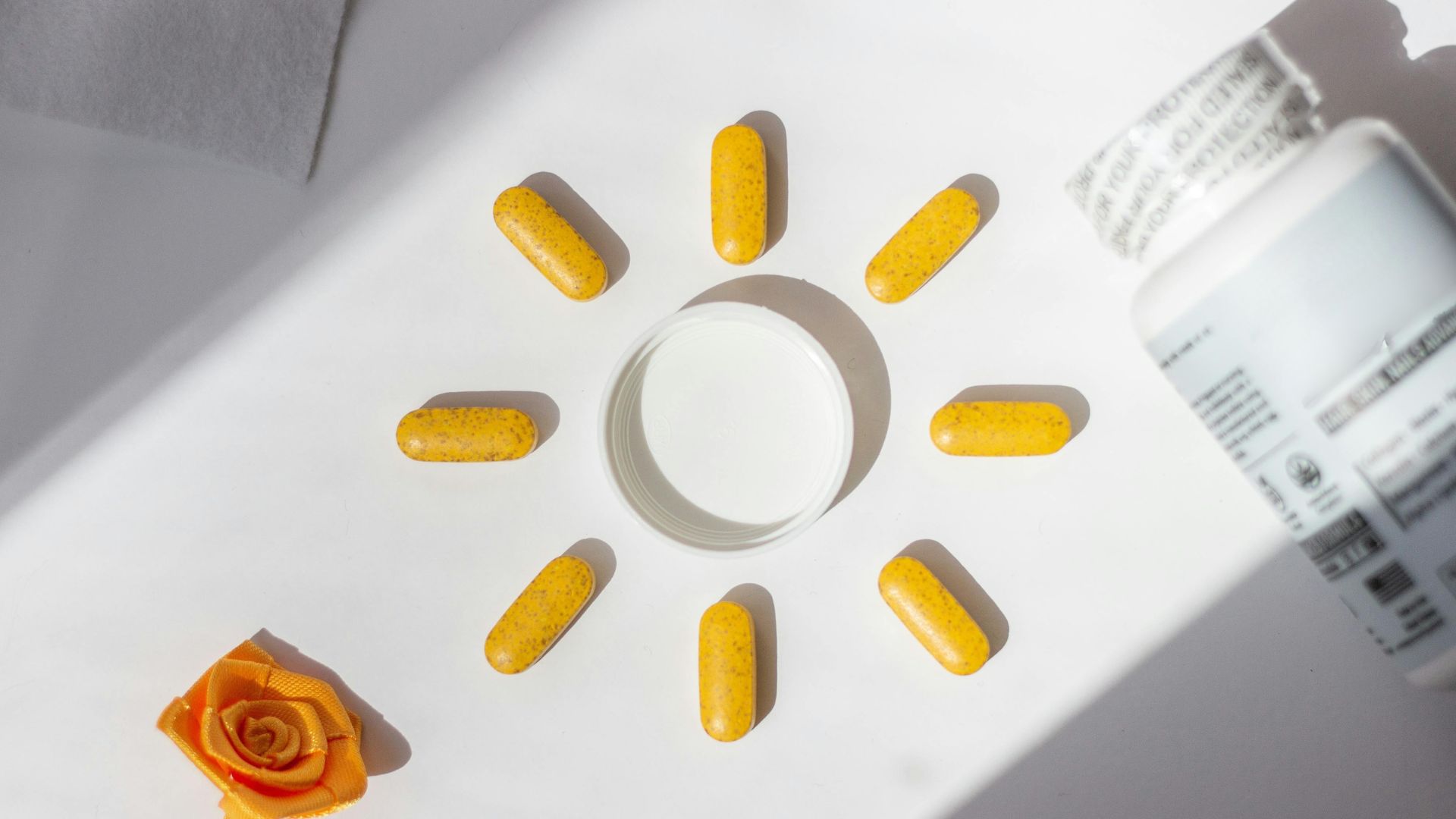 Yellow vitamin tablets arranged in a sun shape beside a supplement bottle, symbolising vitamin D.