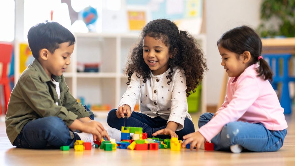 Preschool children sitting on the floor playing with blocks, supporting coordination, balance, and social development.