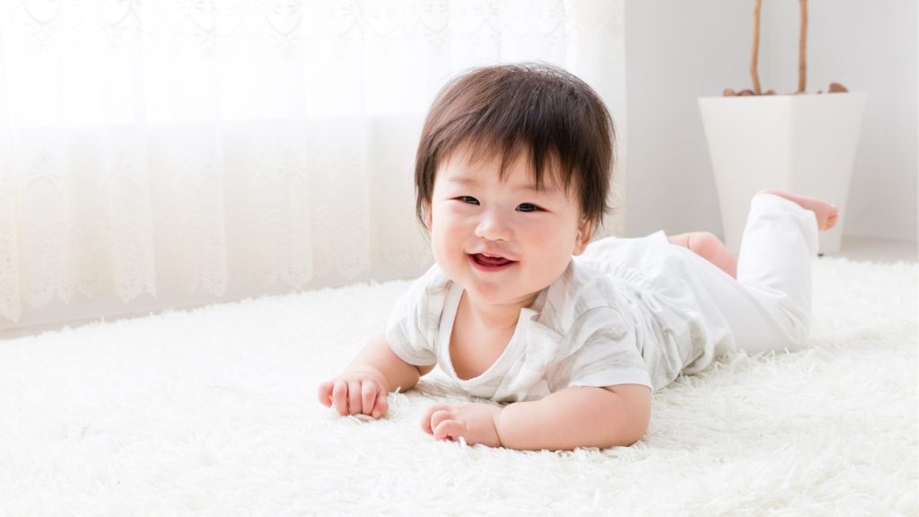 Smiling baby lying on their tummy during tummy time, building neck, arm, and core strength.