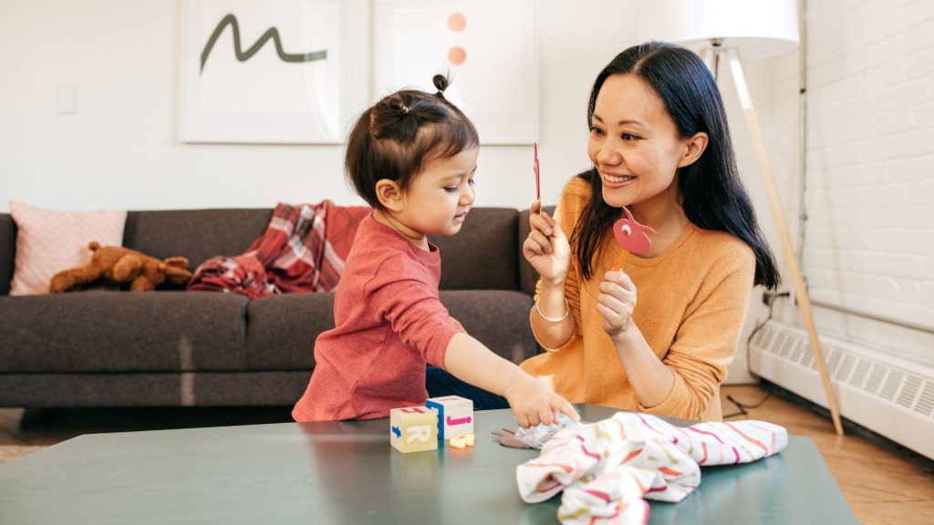 Parent playing with a toddler at home using toys, encouraging learning, coordination, and interaction.