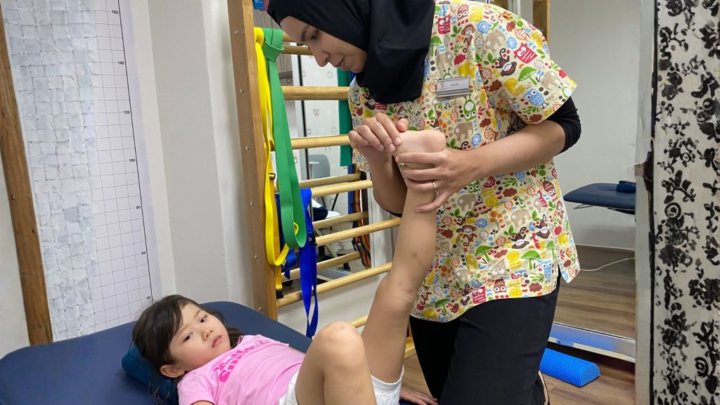 Paediatric physiotherapist assessing a child’s leg and foot movement during a physiotherapy session in a child-friendly clinic.