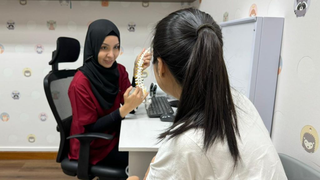 Physiotherapist showing a spine model to a parent while discussing a child’s posture and movement development.