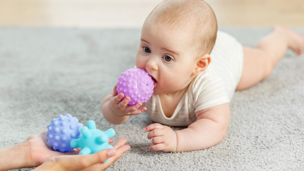 Baby lying on their tummy exploring textured toys, supporting early motor development and sensory exploration.