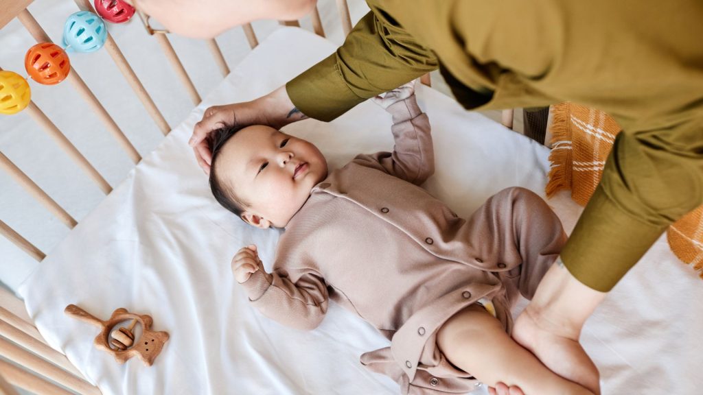 Baby lying comfortably in a cot while a caregiver interacts, observing early movement and responsiveness.