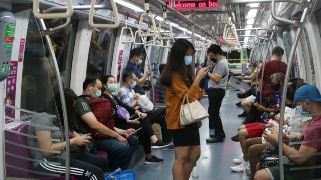 Office commuters standing and sitting inside a Singapore MRT train, illustrating prolonged time spent in enclosed footwear during daily travel.