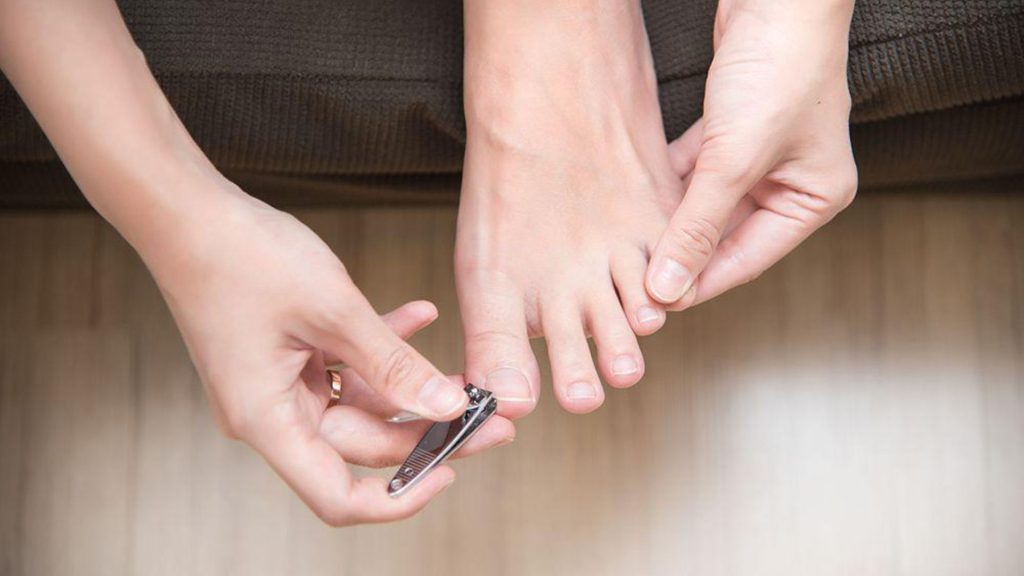 Person trimming their toenails at home, illustrating routine nail care and self-checking for early nail changes