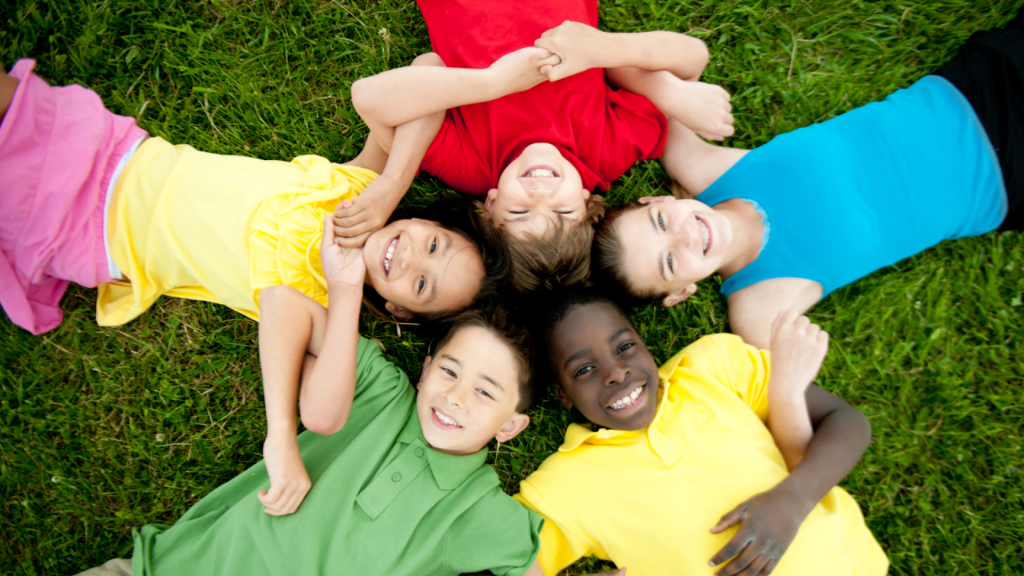 Group of smiling children lying on grass in a circle, representing healthy, active childhood and playful movement.