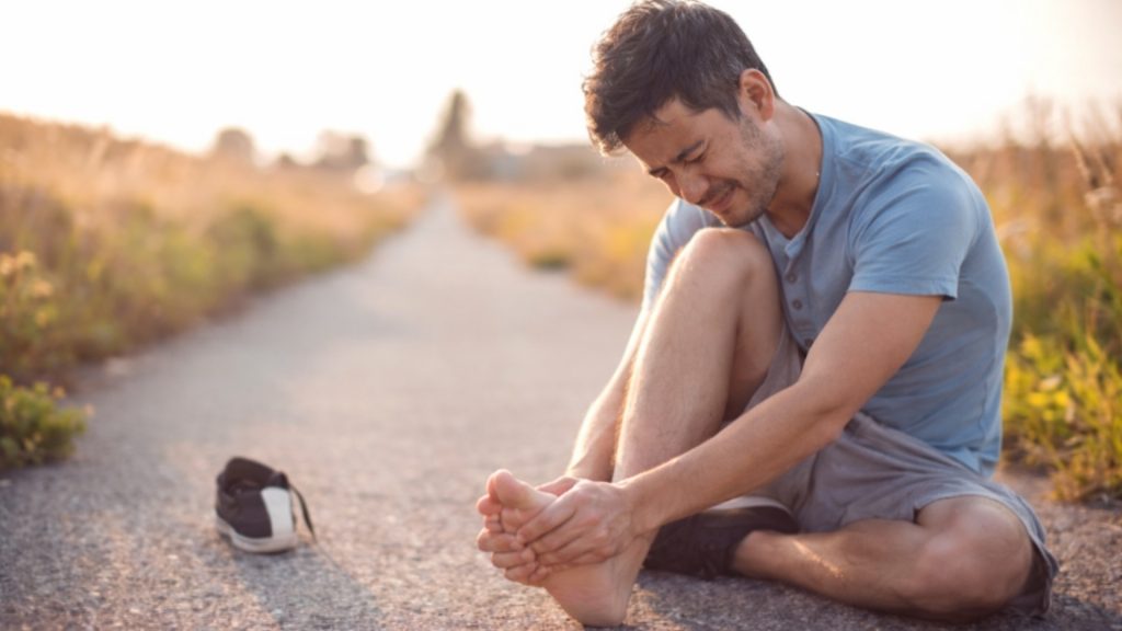Person sitting on a path holding their foot in pain.
