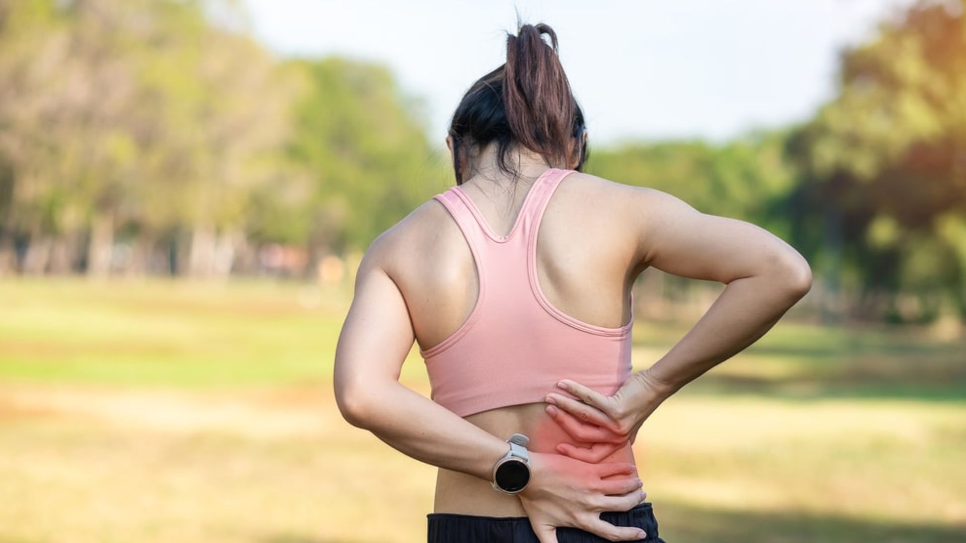 Active adult holding lower back during outdoor exercise, representing lower back pain during physical activity.