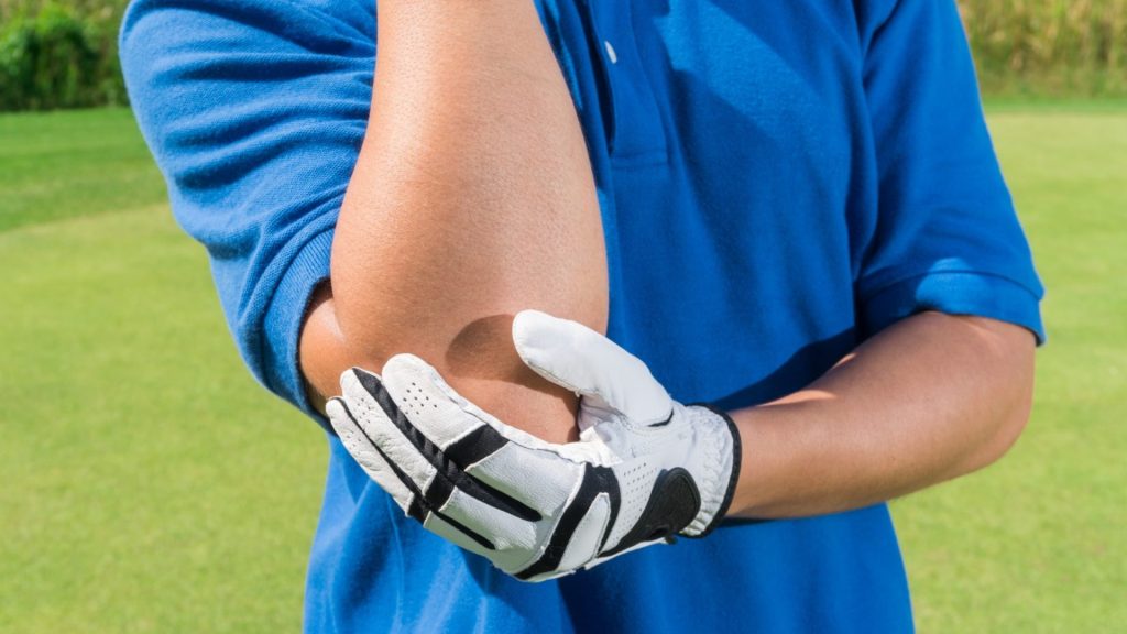 Golfer holding the inner elbow, illustrating elbow pain associated with golfer’s elbow.