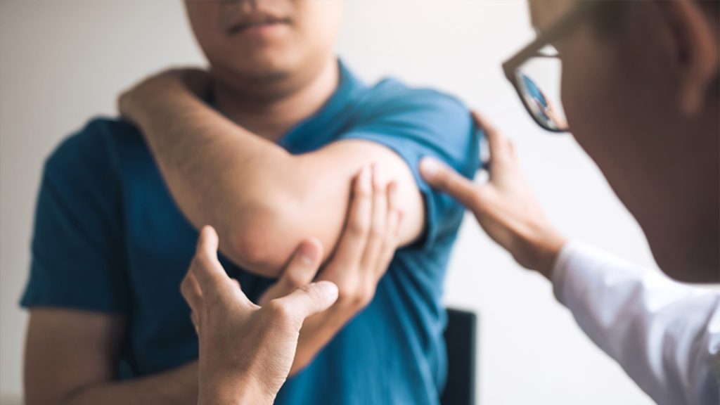 Clinician examining a patient’s elbow to assess pain and movement during a consultation.