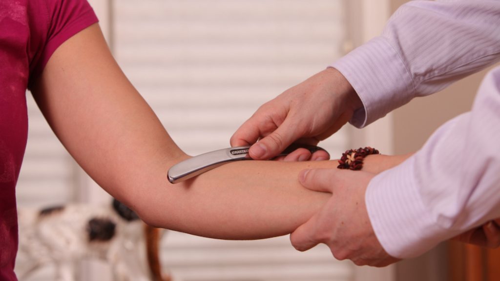 Clinician performing instrument-assisted treatment on a patient’s forearm for elbow pain.